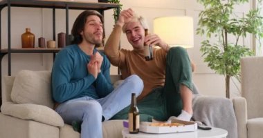 Evde bira içip televizyon izleyen eşcinsel bir çift.