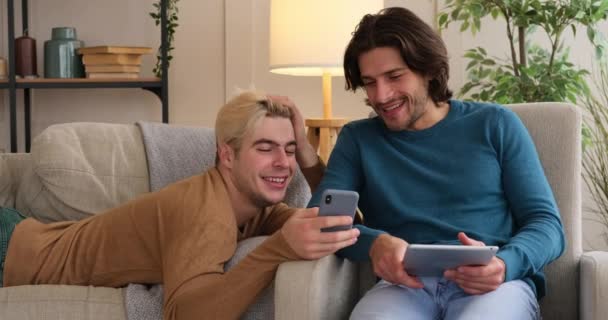 Gay couple using mobile phone and digital tablet at home — Stock Video