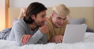 Yatakta dizüstü bilgisayar kullanan eşcinsel çift.