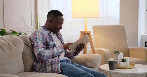 Mężczyzna czyta książkę o kanapie w domu — Wideo stockowe