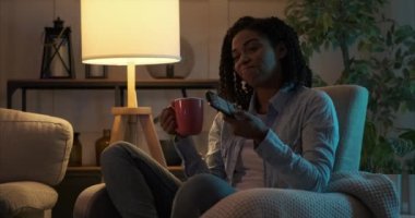 Kadın kanalı değiştirip gece televizyon izliyor.