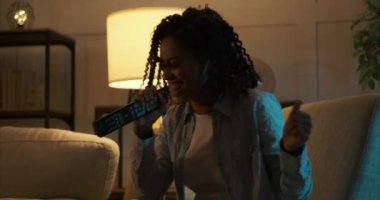 Uzaktan kumandayla şarkı söyleyen ve evinde dans eden bir kadın.