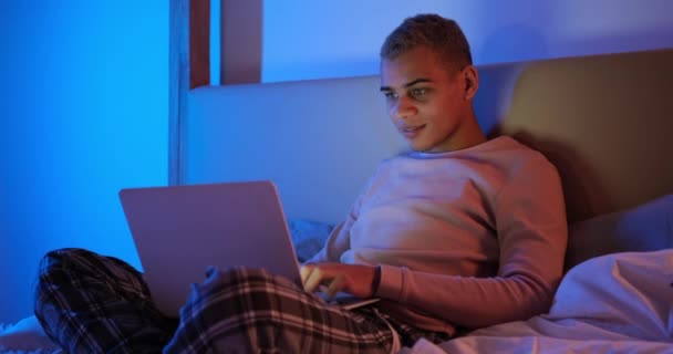 Man lying on bed and using laptop at night — Stock Video