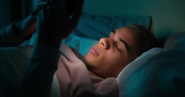 Уставший мужчина использует мобильный телефон поздно ночью в постели — стоковое видео
