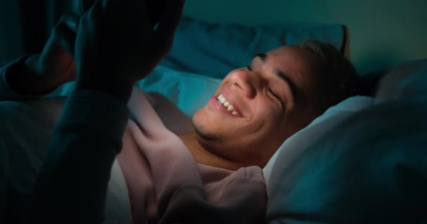 Чоловік за допомогою мобільного телефону лежить на ліжку вночі — стокове відео