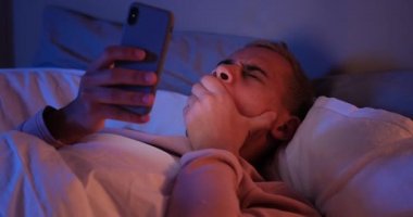 Yatakta cep telefonu kullanan yorgun bir adam.