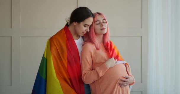 Mujer envuelta en la bandera del arco iris abrazando a su novia embarazada — Vídeos de Stock