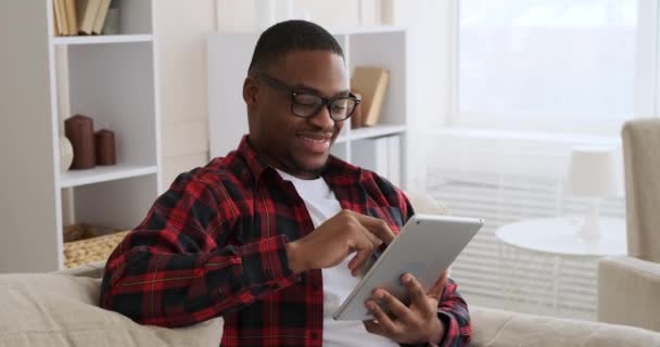 Mężczyzna siedzi na kanapie i używa tabletu cyfrowego — Wideo stockowe