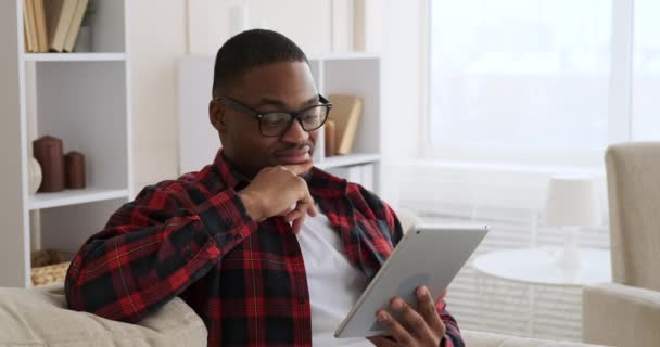 Mężczyzna siedzi na kanapie i używa tabletu cyfrowego — Wideo stockowe