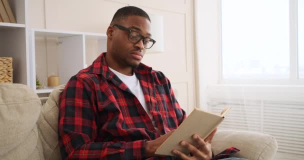 Mann liest Buch zu Hause auf Sofa — Stockvideo