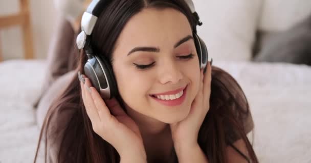 Γυναίκα ξαπλωμένη στο κρεβάτι και ακούγοντας μουσική στα ακουστικά — Αρχείο Βίντεο
