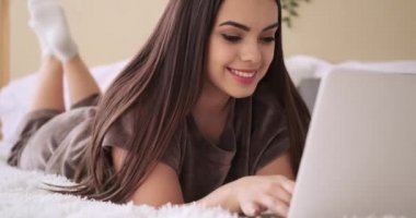 Yatakta dizüstü bilgisayar kullanan mutlu kadın.