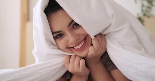 Грайлива жінка стирчить язиком, лежачи на ліжку з ковдрою — стокове відео