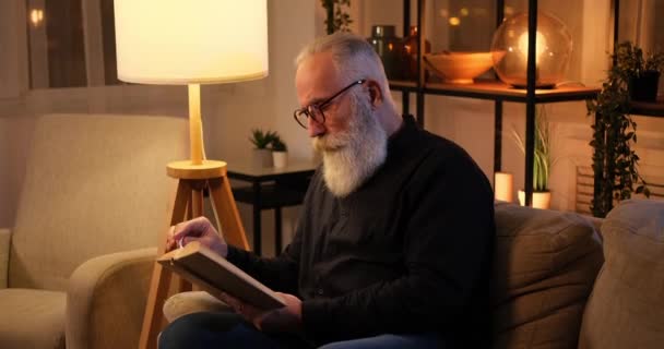 Viejo leyendo un libro hasta tarde en la noche — Vídeos de Stock