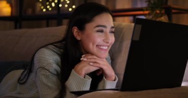 Dizüstü bilgisayarın önünde uzanmış video konferansı yapan bir kadın.