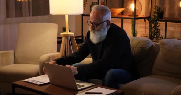 Senior korzystający z laptopa i analizujący dokumenty do późna w nocy — Wideo stockowe