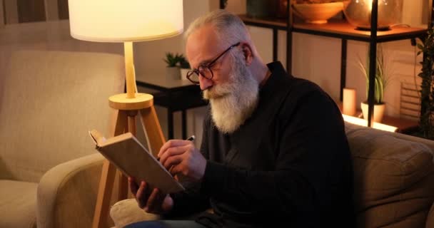 Senior man markering met pen tijdens het lezen van een boek — Stockvideo