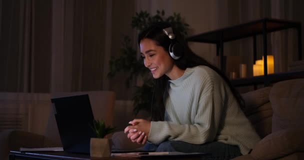 Vrouw met videogesprek met behulp van laptop en koptelefoon laat op de avond — Stockvideo