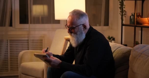 Frustrerad senior man skriva i bok och riva ut papper — Stockvideo