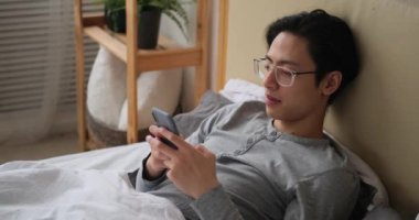 Yatağa yaslanmış cep telefonu kullanan adam.