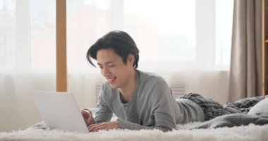 Yatakta dizüstü bilgisayar kullanan mutlu adam.