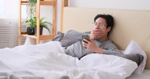 Man yawning and stretching on bed while using mobile phone — Stock Video