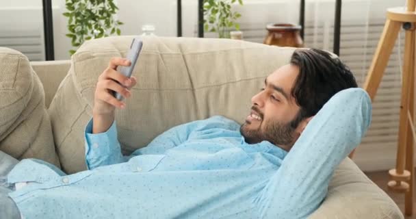 Homem feliz deitado no sofá e usando telefone celular — Vídeo de Stock