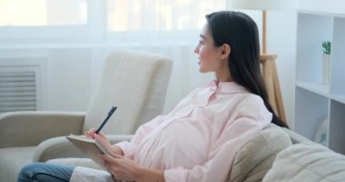Pregnant woman making notes in notebook 