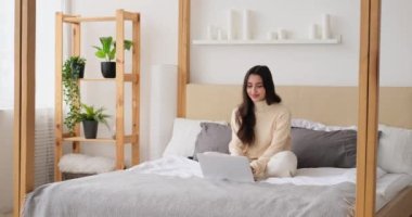 Mutlu kadın yatakta otururken dizüstü bilgisayar kullanıyor.