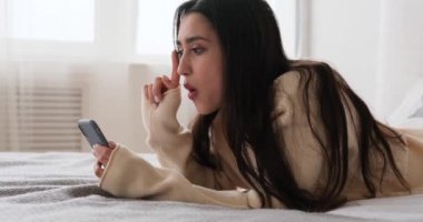 Yatakta cep telefonu kullanan düşünceli bir kadın.