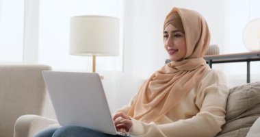 Evdeki koltukta dizüstü bilgisayar kullanan bir kadın.