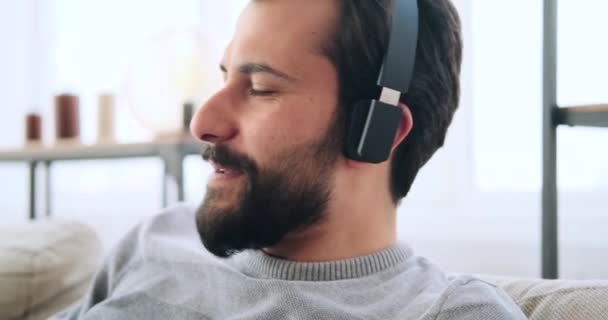 Muž poslech hudby na sluchátka a zpěv při relaxaci na pohovce — Stock video