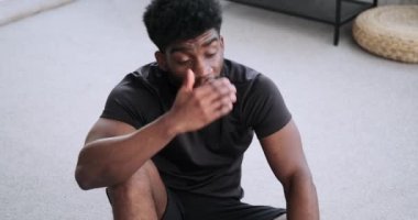 Evde antrenman yaptıktan sonra dinlenirken su içen yorgun bir adam.