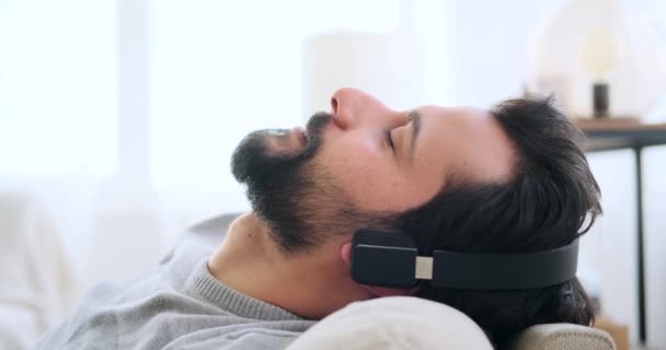 Man die muziek luistert op een koptelefoon terwijl hij op de bank leunt — Stockvideo