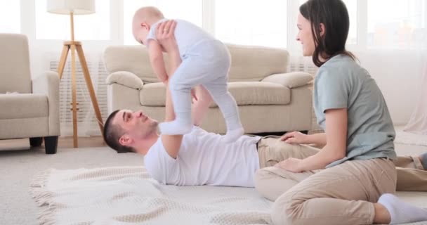 Pais brincando com o bebê filho deitado no tapete em casa — Vídeo de Stock