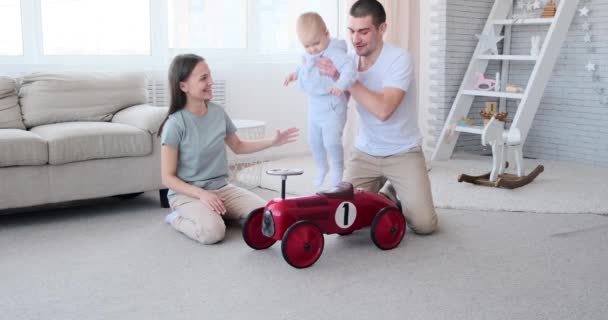 Gelukkig familie met vader duwen baby jongen op speelgoed auto — Stockvideo