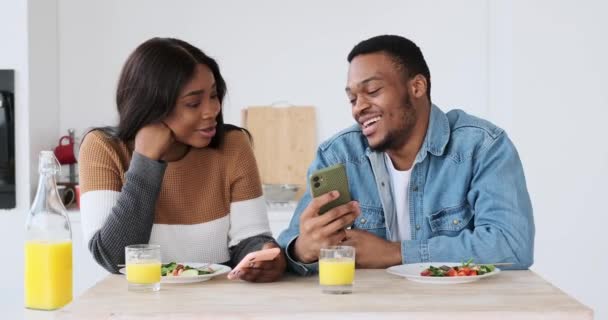 Couple afro-américain montrant et discutant sur téléphone portable tout en déjeunant — Video