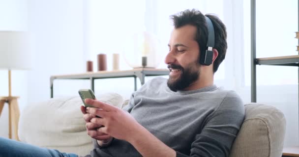 Unge man som använder mobiltelefon när han lyssnar på musik på hörlurar — Stockvideo