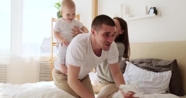 Mãe segurando bebê filho montando na parte de trás do pai na cama — Vídeo de Stock