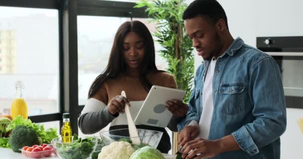 African American ζευγάρι χρησιμοποιώντας ψηφιακή ταμπλέτα κατά την προετοιμασία των τροφίμων στην κουζίνα — Αρχείο Βίντεο