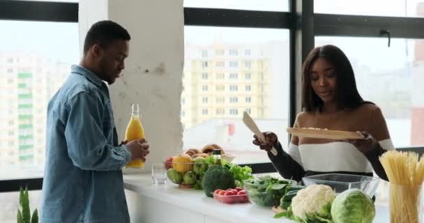 남자가 신선 한 주스를 마시고 아내 가 주방에서 음식을 준비하는 모습 — 비디오
