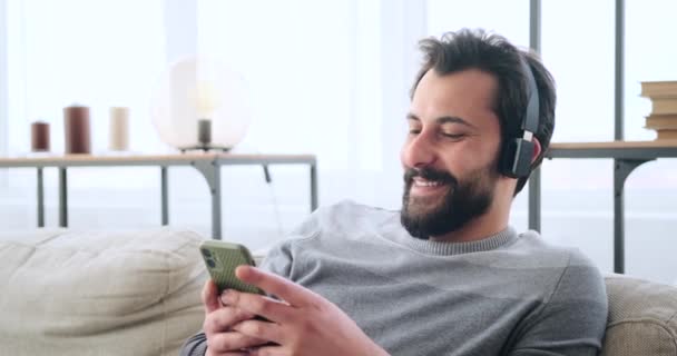 Glad man som använder mobiltelefon när han lyssnar på musik på hörlurar — Stockvideo