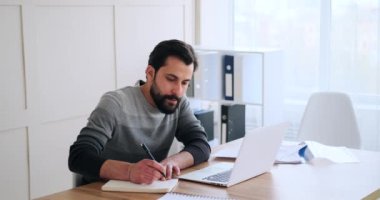 İş adamı dizüstü bilgisayar kullanıyor ve günlüğe notlar yazıyor.