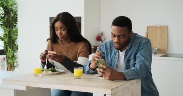 African American ζευγάρι που χρησιμοποιούν το κινητό τηλέφωνο, ενώ έχοντας το μεσημεριανό γεύμα στην κουζίνα — Αρχείο Βίντεο