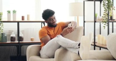 Genç adam koltukta dinlenirken cep telefonu kullanarak kısa mesaj atıyor