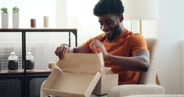 Jeune homme excité déballant de nouvelles chaussures assis sur un fauteuil — Video