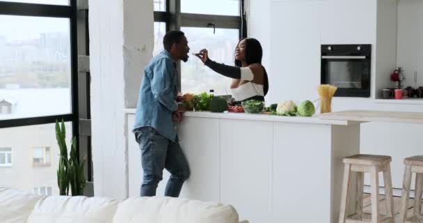 Frau füttert Mann mit Gurke, während er in Küche Essen zubereitet — Stockvideo