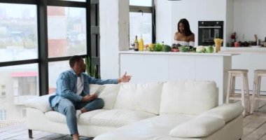 Adam dijital tablet kullanıyor ve karısıyla konuşuyor. Mutfakta yemek hazırlıyor.