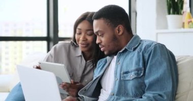 Bilgisayarda çalışan kocasına dijital tablet gösteren bir kadın