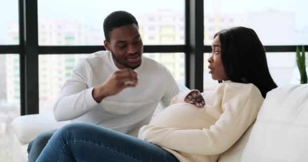 Hombre acariciando vientre de su esposa embarazada sentado en el sofá — Vídeos de Stock
